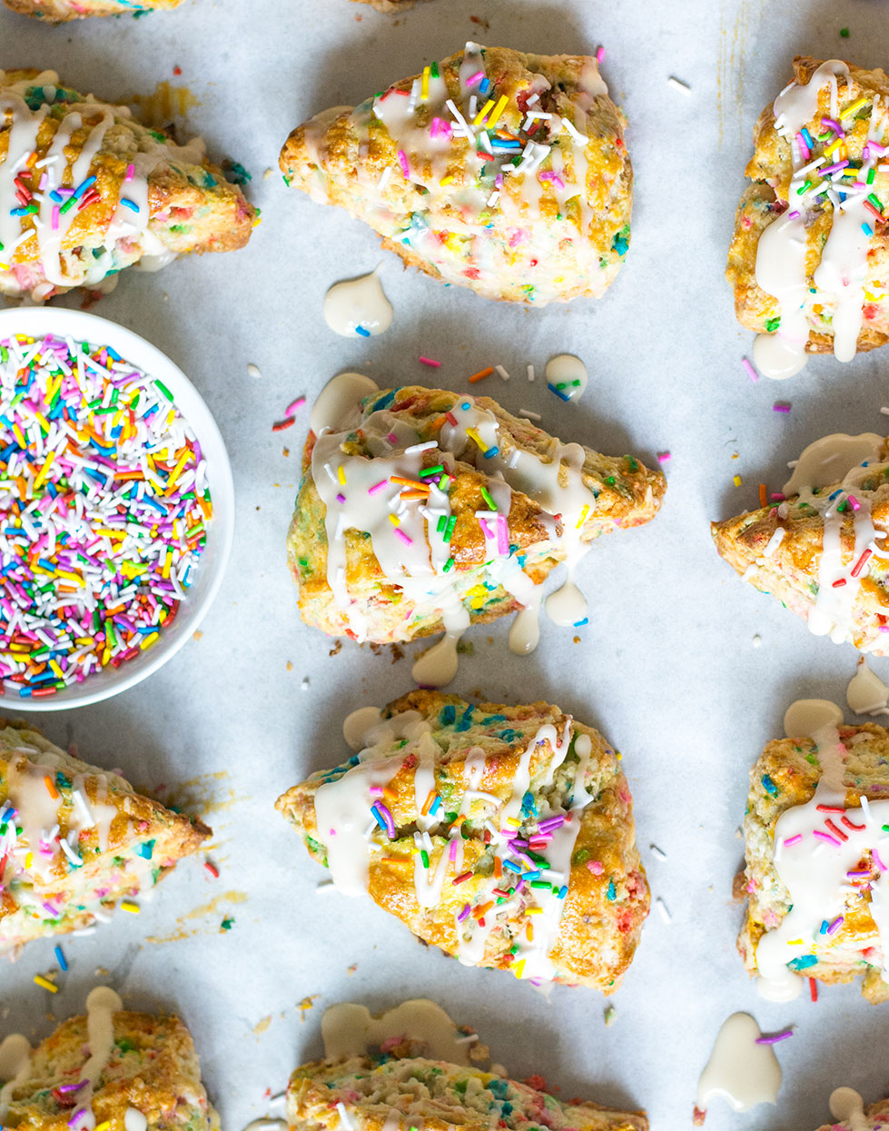 funfetti scones on baking sheet with glaze and sprinkles