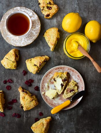top view of a sliced scone on a brown patterned plate with a bowl of lemon curd and scones on a dark background